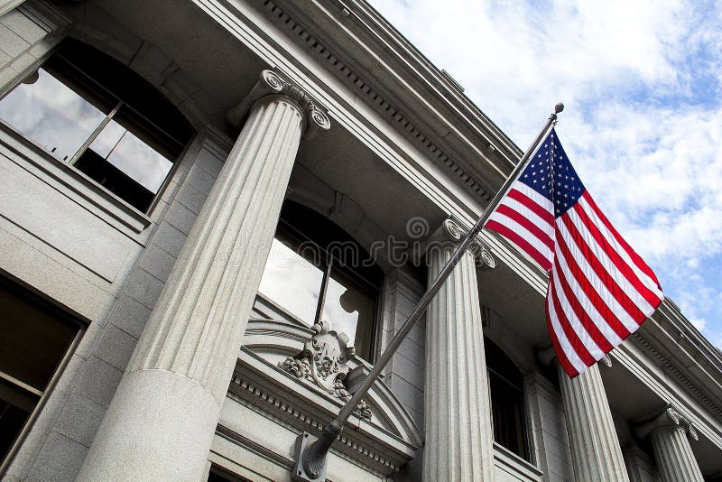 American Flag Blowing in the Wind in Front of Stone Column Building with blue sky and clouds stock photos American Flag Blowing in the Wind in Front of Stone Column Building with blue sky and clouds stock photos