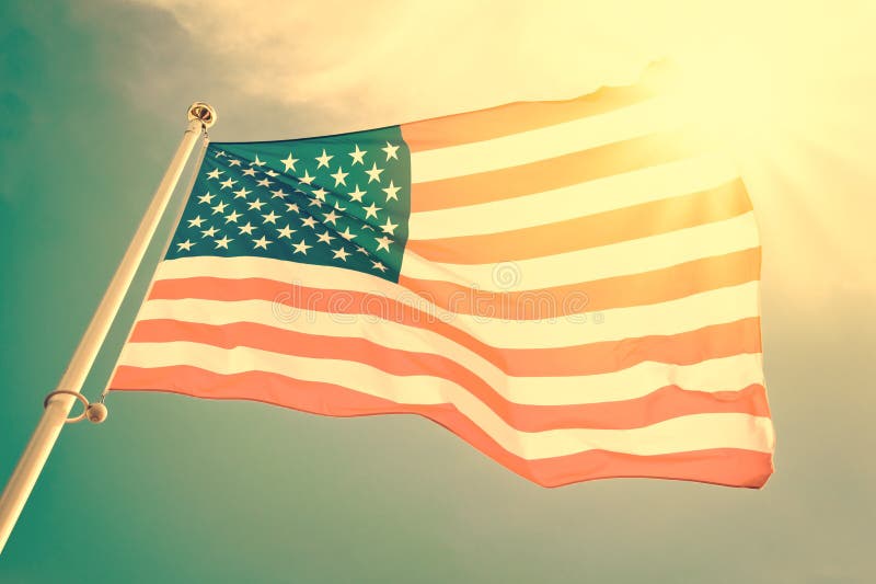 American flag on a pole floating in the wind, sun and blue sky