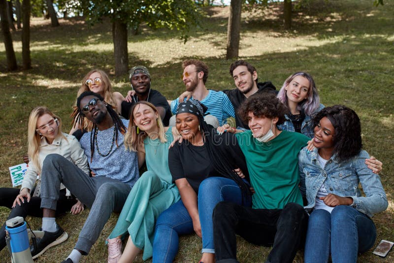 American mixed race youth sit on grass together and have fun, laugh, sing songs and talk with each other. happy young generation