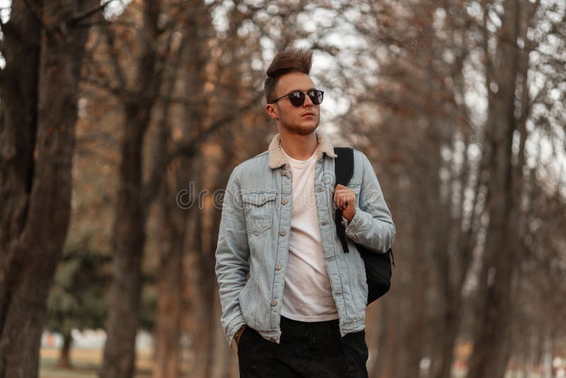 Premium Photo  Nice stylish young hipster man in a denim jacket in a black  t-shirt in sunglasses with a hairstyle stands near a vintage metal red van.  urban trendy guy model