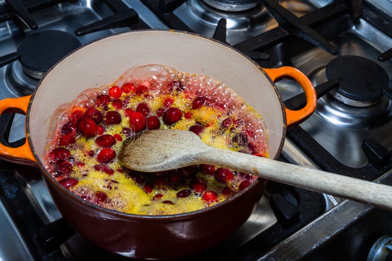 Amerikaanse veenbessen en jus d'orange die worden gekookt om saus met lepel op haardplaat te maken stock foto's Amerikaanse veenbessen en jus d'orange die worden gekookt om saus met lepel op haardplaat te maken stock foto's