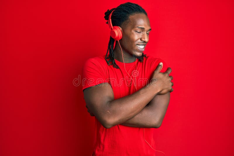 Amerikaner med braider som lyssnar på musik med hörlurar som kramar sig själv, lyckliga och positiva leende självsäkra royaltyfria foton