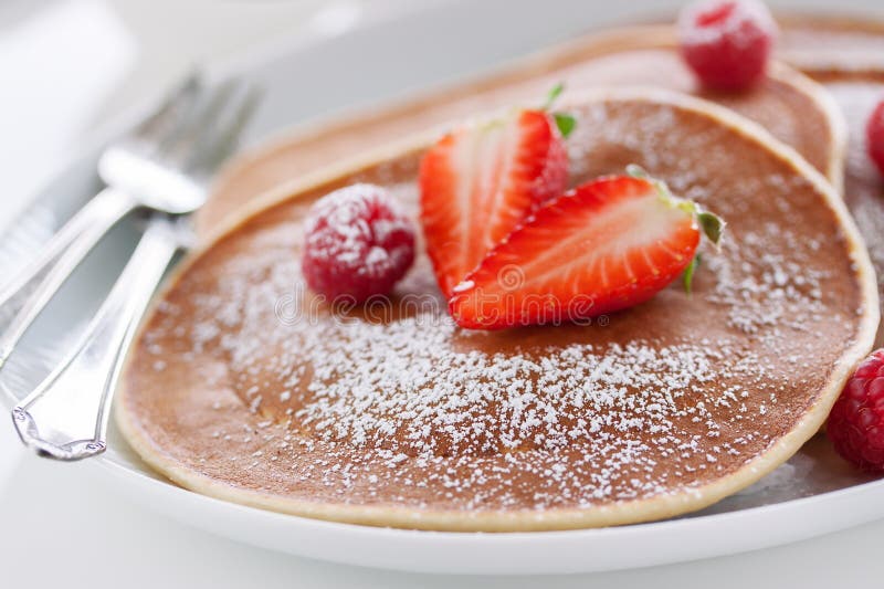 Amerikanska pannkakor för hemlagad kärnmjölk med den nya jordgubben och hallonet på en vit platta royaltyfria foton Amerikanska pannkakor för hemlagad kärnmjölk med den nya jordgubben och hallonet på en vit platta royaltyfria foton