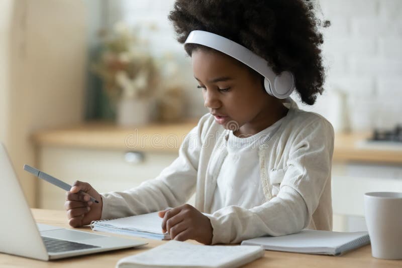 Concentrated little cute african american small child girl in modern wireless headphones sitting in front of computer, checking tasks at online school class, e-learning distant education concept. Concentrated little cute african american small child girl in modern wireless headphones sitting in front of computer, checking tasks at online school class, e-learning distant education concept.