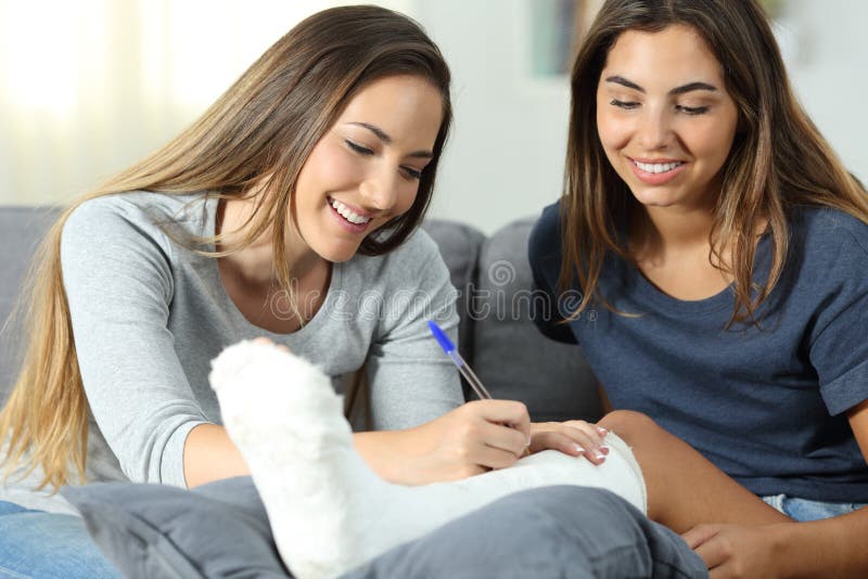 Friend signing in a plaster foot of a disabled women sitting on a couch in the living room at home. Friend signing in a plaster foot of a disabled women sitting on a couch in the living room at home