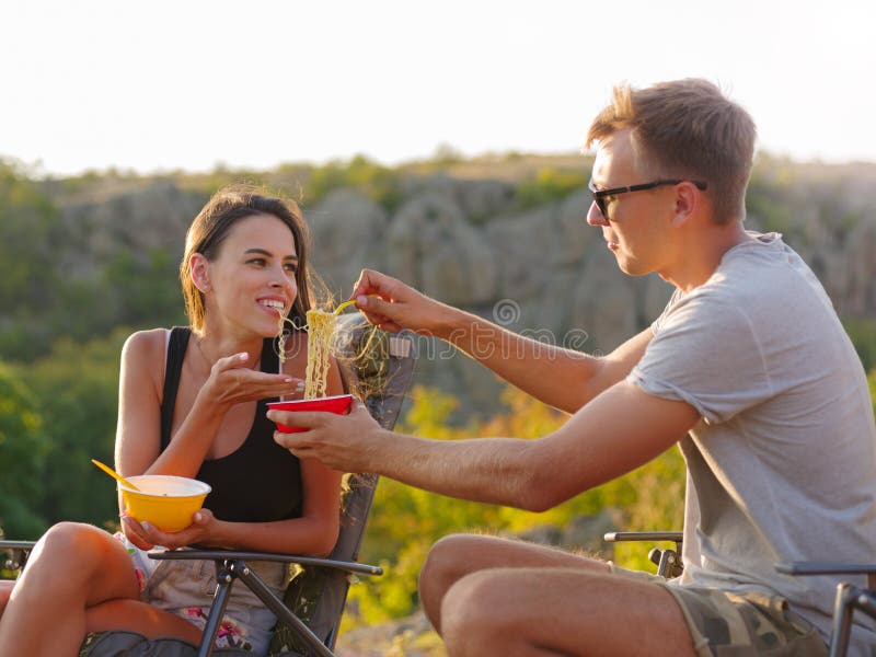 Amica e ragazzo che mangiano le tagliatelle su uno sfondo naturale Divertiresi turistico felice delle coppie Concetto economico d immagini stock Amica e ragazzo che mangiano le tagliatelle su uno sfondo naturale Divertiresi turistico felice delle coppie Concetto economico d immagini stock