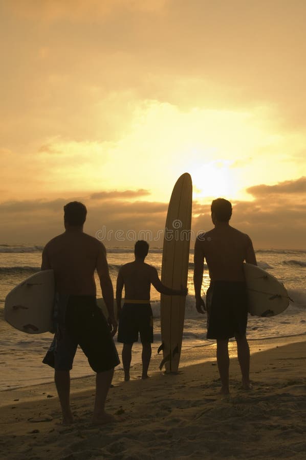 Amici con il tramonto di sorveglianza del surf alla spiaggia fotografia stock libera da diritti Amici con il tramonto di sorveglianza del surf alla spiaggia fotografia stock libera da diritti