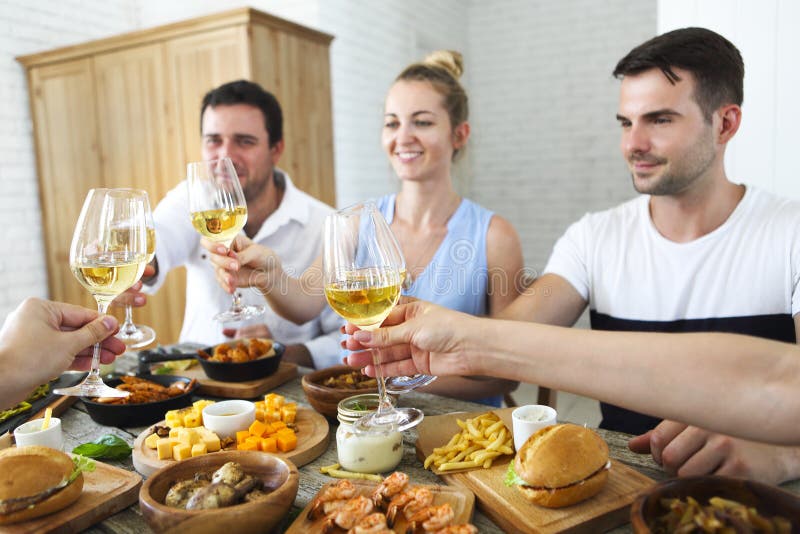 Amici con vino bianco che tostano sopra la tavola servita con alimento fotografia stock libera da diritti Amici con vino bianco che tostano sopra la tavola servita con alimento fotografia stock libera da diritti