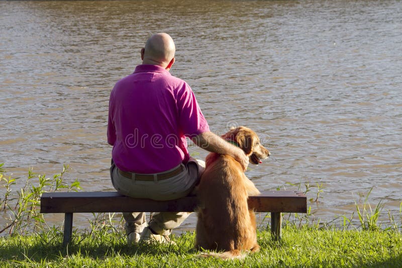 portrait of a mature man sitting in front of a lake hugging his golden retriever dog in a cuddling moment. portrait of a mature man sitting in front of a lake hugging his golden retriever dog in a cuddling moment