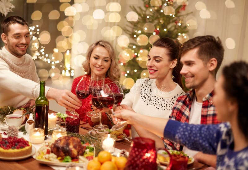 Holidays and celebration concept - happy friends having christmas dinner at home, drinking red wine and clinking glasses. Holidays and celebration concept - happy friends having christmas dinner at home, drinking red wine and clinking glasses