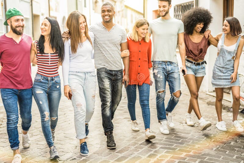 Amici millenari multirazziali che camminano e che parlano nel centro urbano immagini stock Amici millenari multirazziali che camminano e che parlano nel centro urbano immagini stock