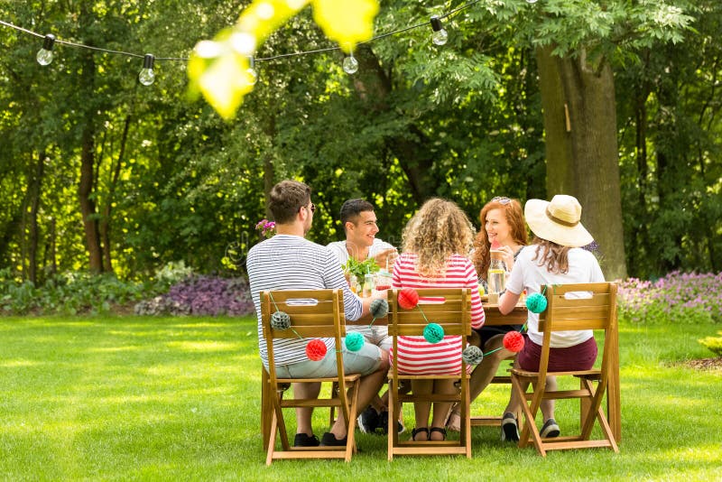 Amici multiculturali che si siedono alla tavola e che parlano in GA immagine stock libera da diritti Amici multiculturali che si siedono alla tavola e che parlano in GA immagine stock libera da diritti