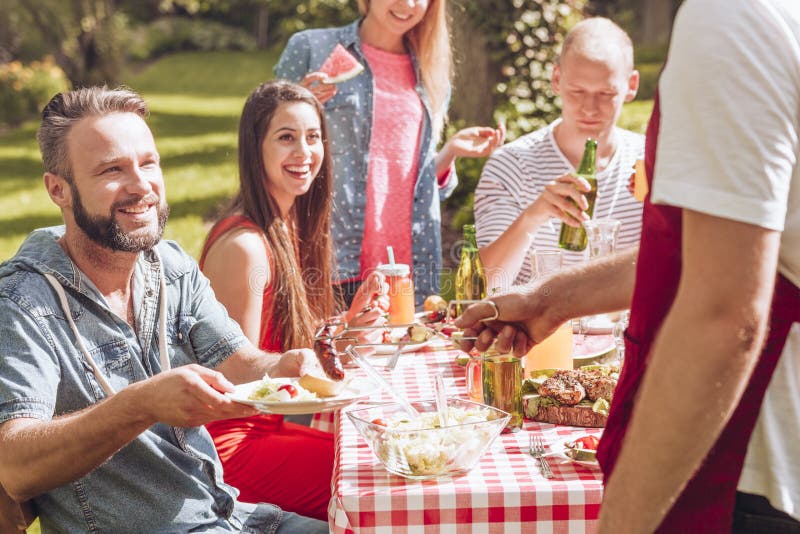 Amici sorridenti che mangiano alimento arrostito durante la festa di compleanno nel giardino fotografie stock libere da diritti Amici sorridenti che mangiano alimento arrostito durante la festa di compleanno nel giardino fotografie stock libere da diritti
