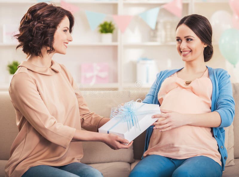 Friend Giving to Pregnant Woman Gift in Blue Box. Happy Pregnant Mother in Bedroom at Home. Pregnancy and Motherhood Concept. Young Mother Expecting Baby Concept. Friendship Concept. Friend Giving to Pregnant Woman Gift in Blue Box. Happy Pregnant Mother in Bedroom at Home. Pregnancy and Motherhood Concept. Young Mother Expecting Baby Concept. Friendship Concept.