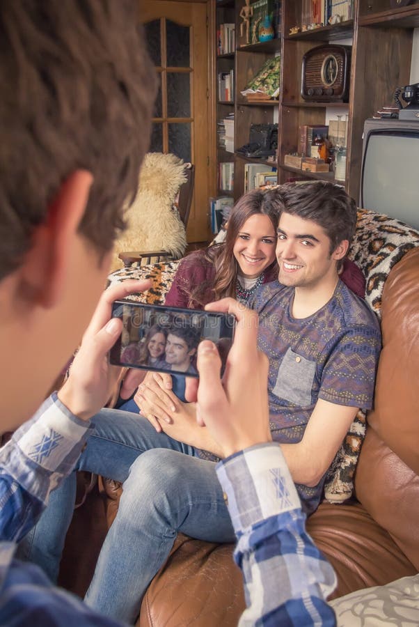 Amico che prende le foto alle coppie adolescenti su un sofà immagini stock libere da diritti Amico che prende le foto alle coppie adolescenti su un sofà immagini stock libere da diritti
