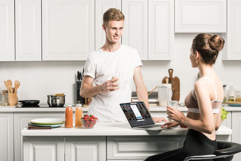 girlfriend using laptop with loaded linkedin page and looking at boyfriend in kitchen. girlfriend using laptop with loaded linkedin page and looking at boyfriend in kitchen