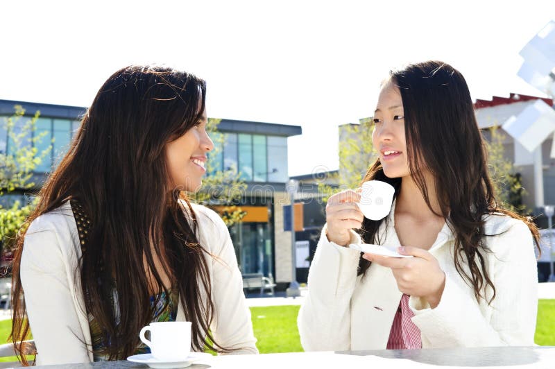 Two girl friends sitting and having drinks at outdoor mall. Two girl friends sitting and having drinks at outdoor mall