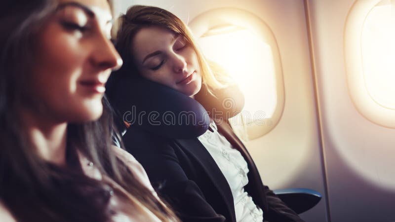 Girlfriends traveling by plane. A female passenger sleeping on neck cushion in airplane. Girlfriends traveling by plane. A female passenger sleeping on neck cushion in airplane