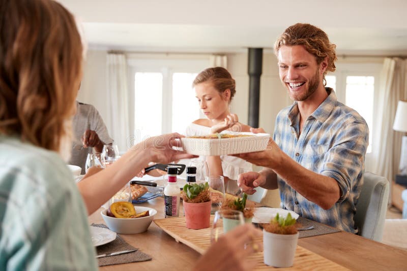 Amigos adultos jovenes que se sirven el almuerzo en una tabla de cena, cierre para arriba fotos de archivo libres de regalías Amigos adultos jovenes que se sirven el almuerzo en una tabla de cena, cierre para arriba fotos de archivo libres de regalías