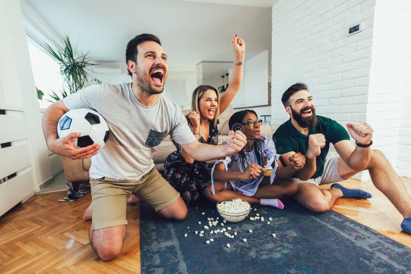 Grupo diversificado de amigos assistindo jogos esportivos em casa e  apostando online