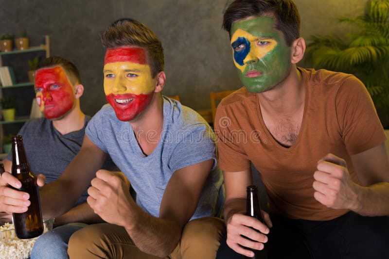 Amigos com caras coloridas que olham o futebol imagens de stock Amigos com caras coloridas que olham o futebol imagens de stock