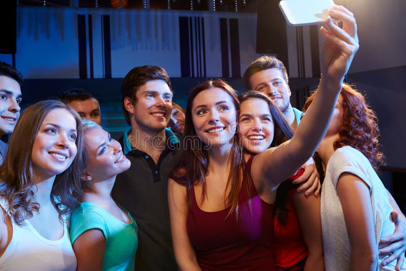 Party, technology, nightlife and people concept - smiling friends with smartphone taking selfie in club. Party, technology, nightlife and people concept - smiling friends with smartphone taking selfie in club