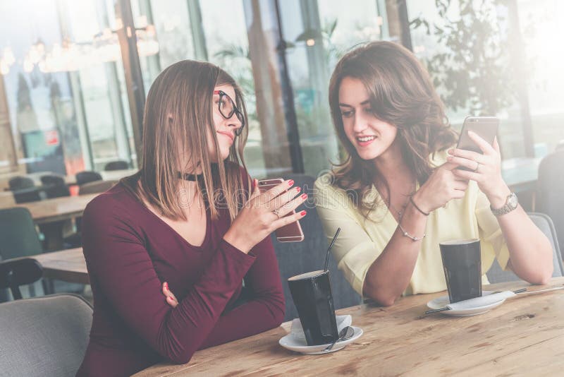 Amigos da reunião em um café Duas meninas alegres sentam-se em uma tabela, bebem-se o café e discutem-se a notícia imagens de stock royalty free Amigos da reunião em um café Duas meninas alegres sentam-se em uma tabela, bebem-se o café e discutem-se a notícia imagens de stock royalty free