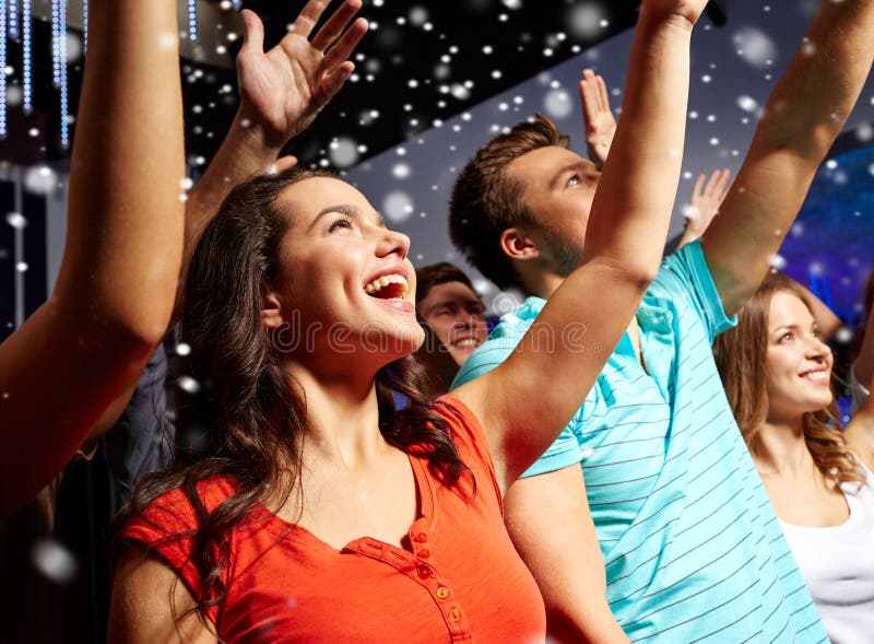 Party, holidays, celebration, nightlife and people concept - smiling friends waving hands at concert in club and snow effect. Party, holidays, celebration, nightlife and people concept - smiling friends waving hands at concert in club and snow effect