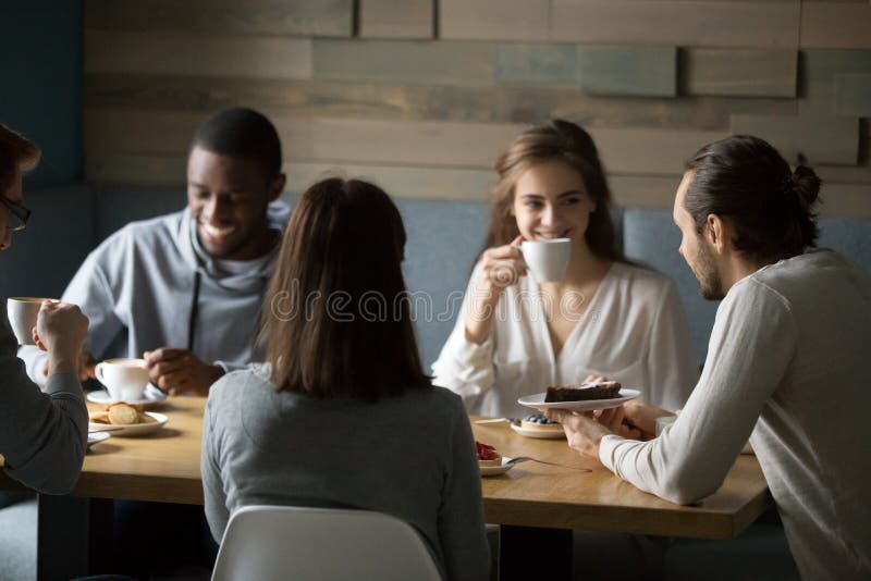 Amigos diversos de sorriso que apreciam o café e as sobremesas no café imagens de stock royalty free Amigos diversos de sorriso que apreciam o café e as sobremesas no café imagens de stock royalty free