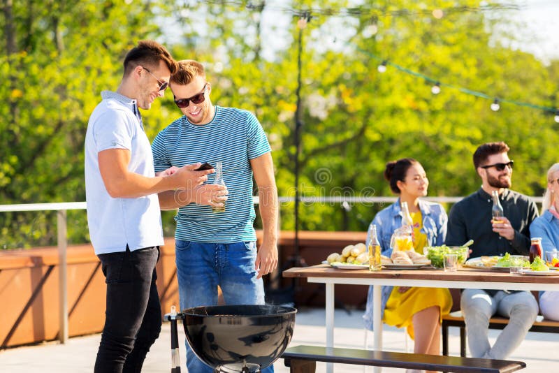 Amigos felices que asan a la parrilla en el partido del Bbq en tejado fotografía de archivo libre de regalías Amigos felices que asan a la parrilla en el partido del Bbq en tejado fotografía de archivo libre de regalías