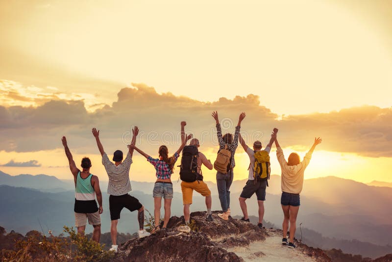 Group of happy friends stands with raised arms at sunset mountain and enjoys sunset. Group of happy friends stands with raised arms at sunset mountain and enjoys sunset