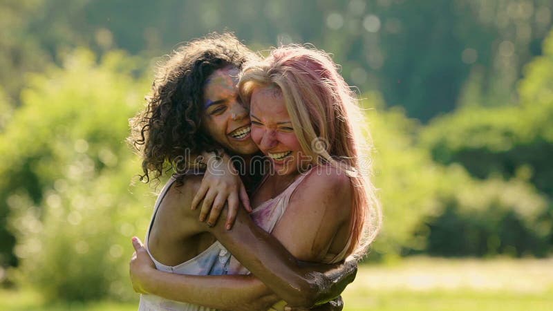 Amigos femeninos felices que abrazan y que se ríen del festival del color del verano, cámara lenta