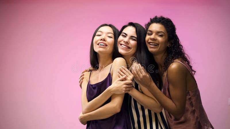 Amigos femeninos que abrazan y que presentan para la cámara en el fondo rosado, partido de pijama fotografía de archivo Amigos femeninos que abrazan y que presentan para la cámara en el fondo rosado, partido de pijama fotografía de archivo
