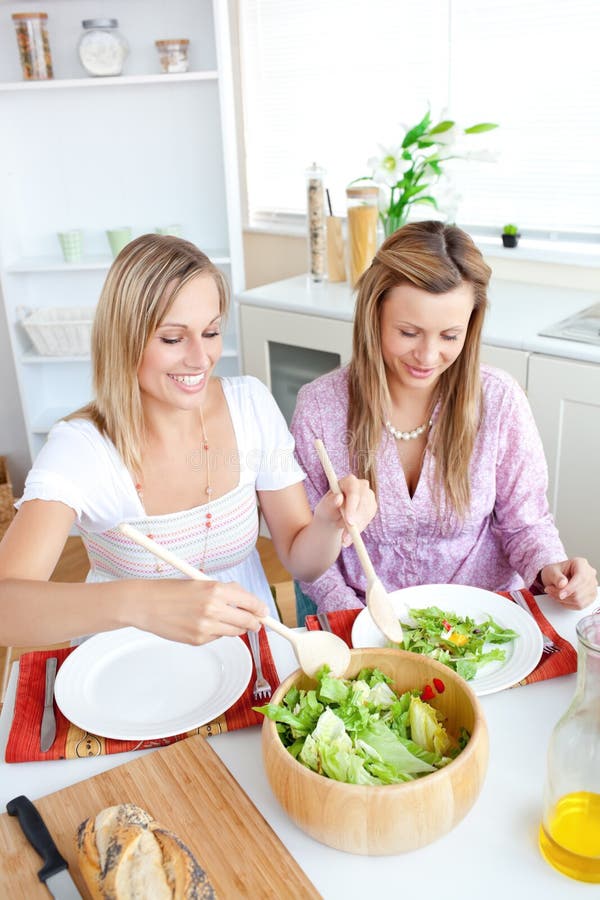 Amigos femeninos que brillan intensamente que comen la ensalada en la cocina imagenes de archivo Amigos femeninos que brillan intensamente que comen la ensalada en la cocina imagenes de archivo