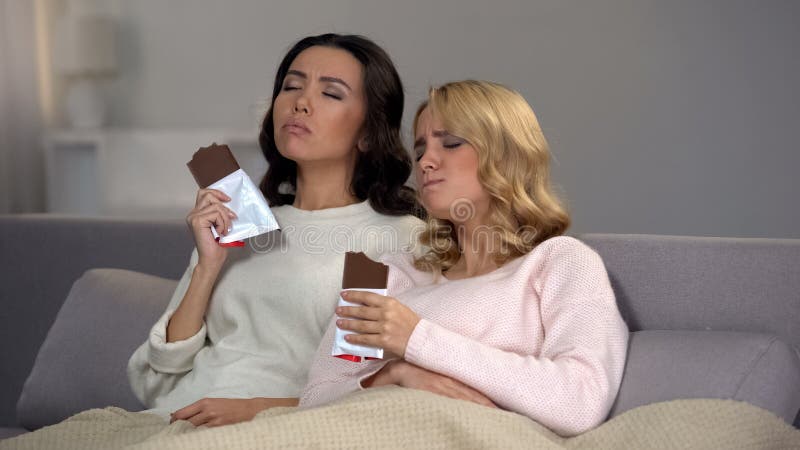 Amigos femeninos que se sientan en el sof? y que disfrutan del gusto del chocolate dulce, hormonas