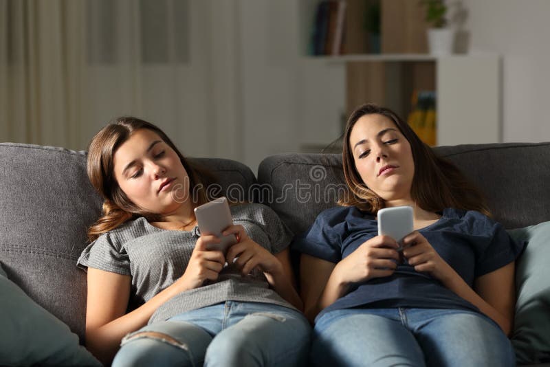 Bored friends using their smart phones sitting on a couch in the living room at home. Bored friends using their smart phones sitting on a couch in the living room at home