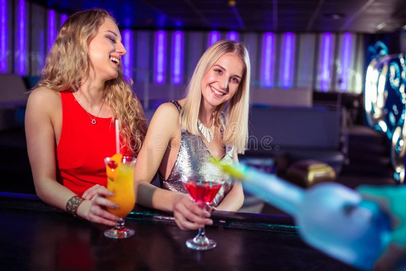 Amigos fêmeas novos que apreciam bebidas no clube noturno imagem de stock royalty free Amigos fêmeas novos que apreciam bebidas no clube noturno imagem de stock royalty free