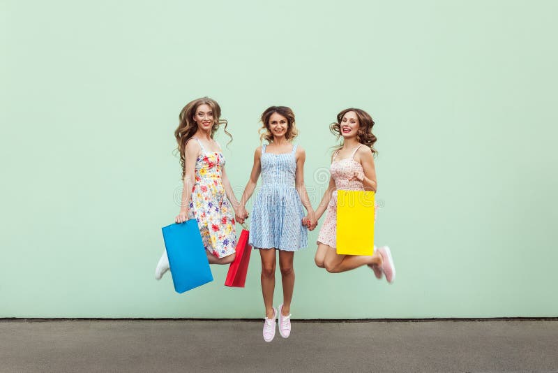 Amigos hermosos de la felicidad tres que saltan de feliz con los paquetes coloridos después de hacer compras fotos de archivo libres de regalías Amigos hermosos de la felicidad tres que saltan de feliz con los paquetes coloridos después de hacer compras fotos de archivo libres de regalías