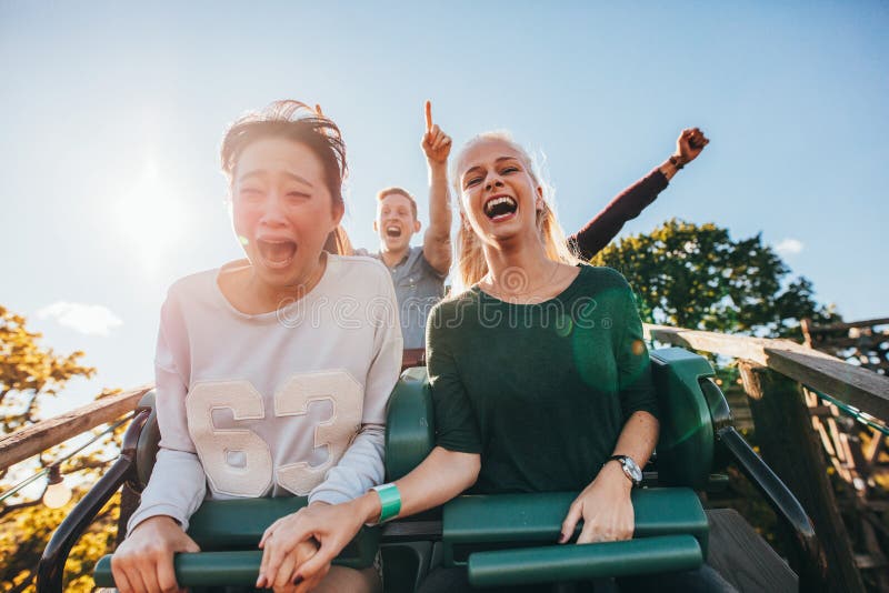 Amigos jovenes entusiastas que montan paseo del parque de atracciones foto de archivo Amigos jovenes entusiastas que montan paseo del parque de atracciones foto de archivo