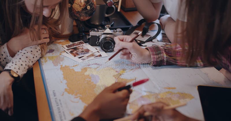 Amigos jovens felizes e diversificados estudam e olham em cima da mesa da cozinha com o mapa mundial planejando viagens em câmera