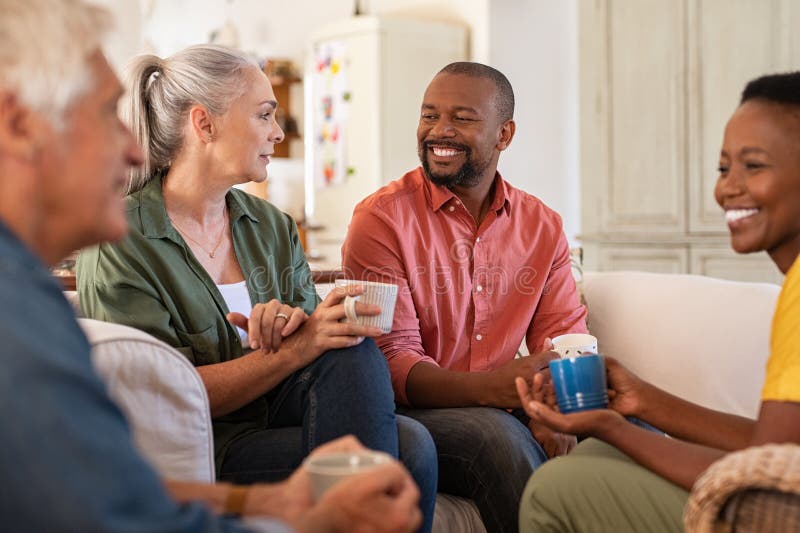 Senior and mature couples in conversation at home. Cheerful multiethnic group of people enjoying a cup of tea while talking to each other. Group of senior people socializing over coffee. Senior and mature couples in conversation at home. Cheerful multiethnic group of people enjoying a cup of tea while talking to each other. Group of senior people socializing over coffee