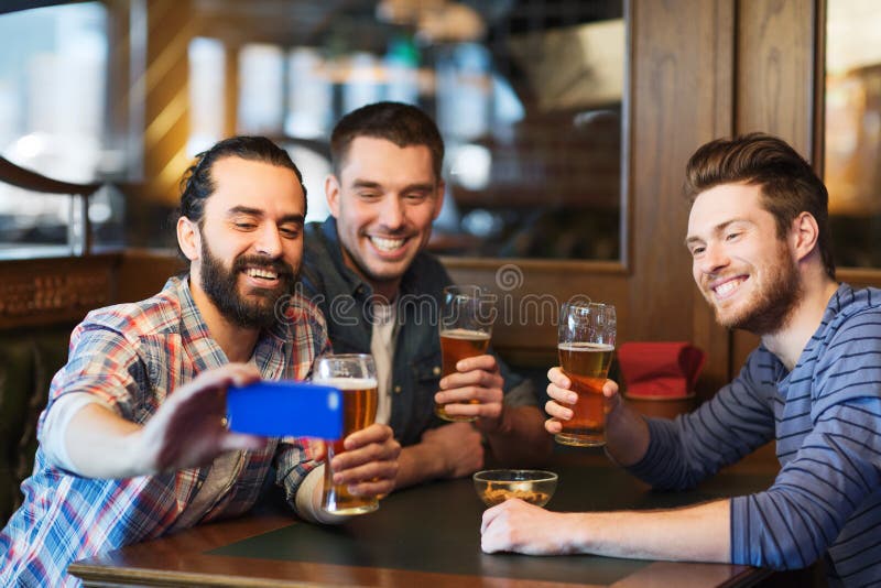 Amigos masculinos com cerveja bebendo do smartphone na barra foto de stock Amigos masculinos com cerveja bebendo do smartphone na barra foto de stock