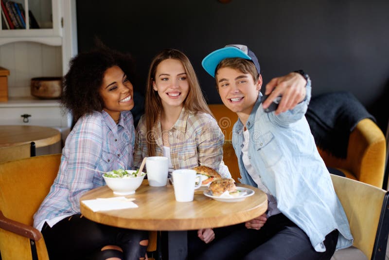 Amigos multirraciais alegres que tomam o selfie em um café imagem de stock royalty free Amigos multirraciais alegres que tomam o selfie em um café imagem de stock royalty free