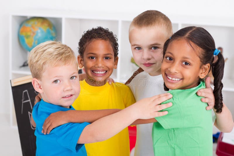 Four happy diverse preschool friends hugging in a circle in classroom. Four happy diverse preschool friends hugging in a circle in classroom