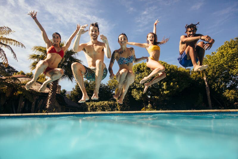 Group of multi-ethnic young people looking happy while jumping into the swimming pool together. Friends enjoying pool party. Group of multi-ethnic young people looking happy while jumping into the swimming pool together. Friends enjoying pool party.