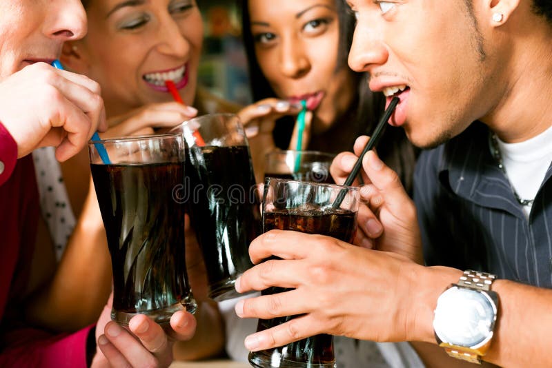 Amigos que bebem a soda em uma barra