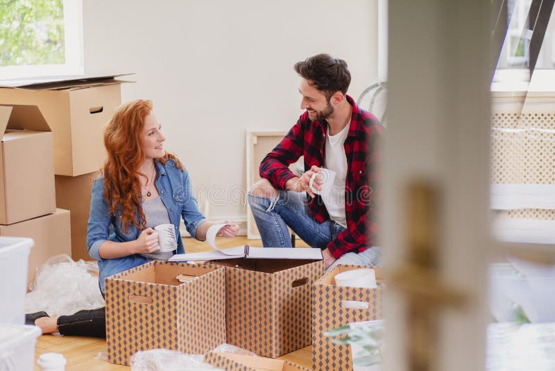 Amigos sonrientes que desempaquetan la materia y que beben el café en el interior con las cajas fotos de archivo libres de regalías Amigos sonrientes que desempaquetan la materia y que beben el café en el interior con las cajas fotos de archivo libres de regalías
