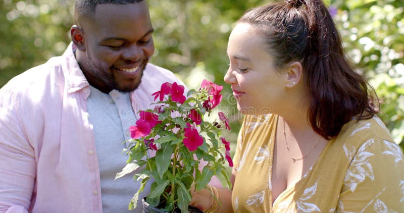 Amis afro-américains et caucasiennes sentant des fleurs dans le jardin clips vidéos