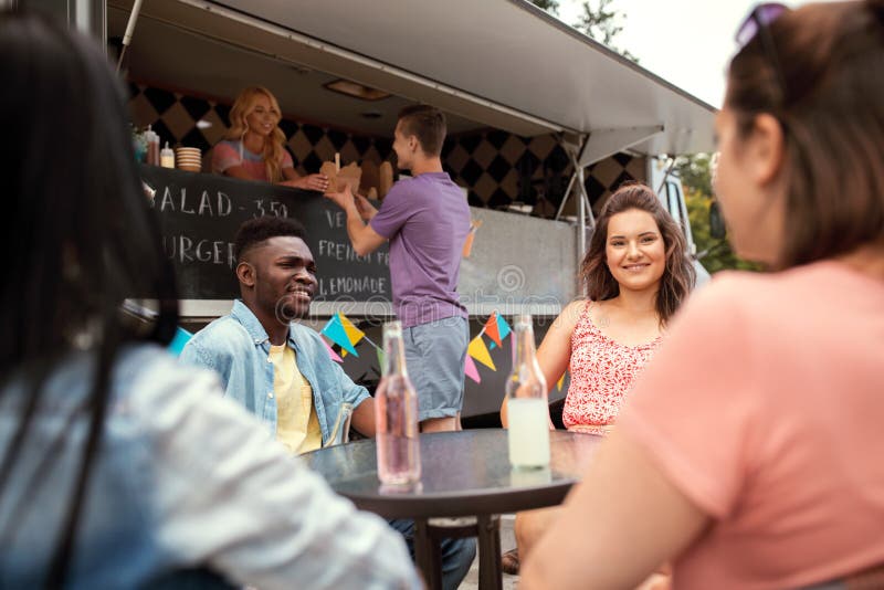 Amis avec des boissons se reposant à la table au camion de nourriture image stock Amis avec des boissons se reposant à la table au camion de nourriture image stock