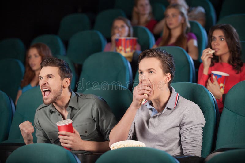 Two friends watching movie at the cinema with people on the background. Two friends watching movie at the cinema with people on the background